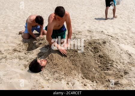 Der kleine Junge wird von seinen Freunden am Strand in İstanbul im Sand begraben. Im Sand begraben. Stockfoto