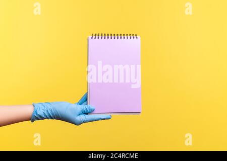 Profil Seitenansicht Nahaufnahme der menschlichen Hand in blauen chirurgischen Handschuhe mit lila Notizblock in der Hand und hält leeres Papier. Indoor, Studio-Aufnahme, isoliert Stockfoto