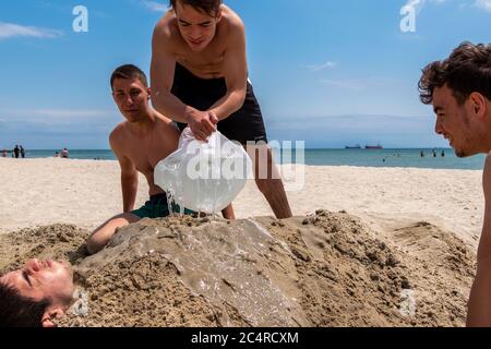 Der kleine Junge wird von seinen Freunden am Strand in İstanbul im Sand begraben. Im Sand begraben. Stockfoto