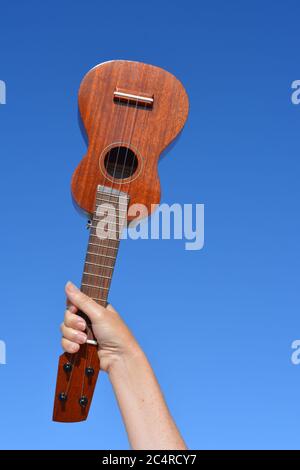 Sopranukulele hielt sich in der Hand einer Frau gegen den blauen Himmel, mit Kopierraum Stockfoto