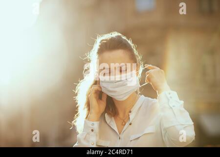 Leben während Coronavirus Pandemie. Trendige Frau in blauer Bluse im Freien auf der Straße der Stadt trägt medizinische Maske. Stockfoto