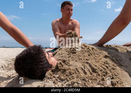 Der kleine Junge wird von seinen Freunden am Strand in İstanbul im Sand begraben. Im Sand begraben. Stockfoto