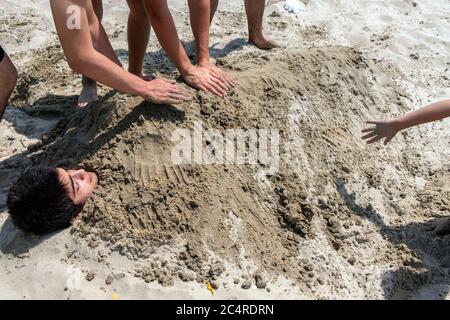 Der kleine Junge wird von seinen Freunden am Strand in İstanbul im Sand begraben. Im Sand begraben. Stockfoto