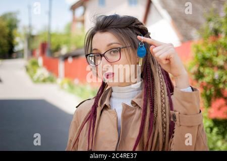 Modernes junges Mädchen mit langen Dreadlocks und Brillen zeigt Haufen Hausschlüssel in einer Hand in Richtung der Kamera. Immobilienmakler Konzept Stockfoto