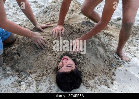 Der kleine Junge wird von seinen Freunden am Strand in İstanbul im Sand begraben. Im Sand begraben. Stockfoto