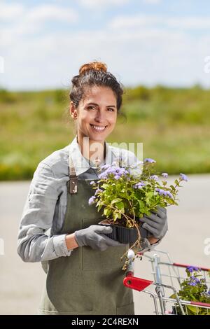 Vertikale Taille oben Porträt von lächelnden weiblichen Gärtner hält Blumentöpfe Blick auf Kamera, während Sie mit dem Wagen im Freien, kopieren Raum Stockfoto