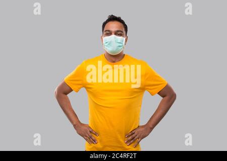 Indian man Hände an Seiten tragen medizinische Maske in Gelb Tshirt isoliert Stockfoto