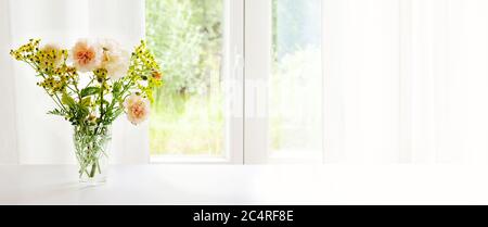 Blumenstrauß aus orangen Rosen und Raute in Glasvase am Fenster vor einem weißen Vorhang, Panoramafenster, großer Kopierraum, ausgewählter Fokus Stockfoto