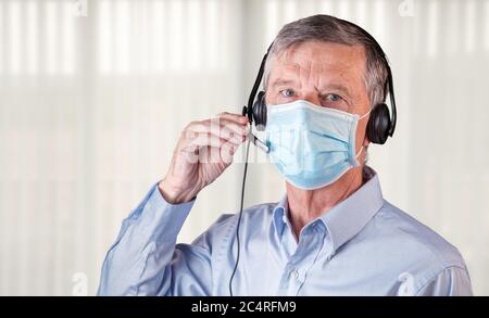 Leitender Kaukasusmann mit Gesichtsmask und Headset, um während der Coronavirus-Epidemie mit Kunden oder Team zu sprechen Stockfoto