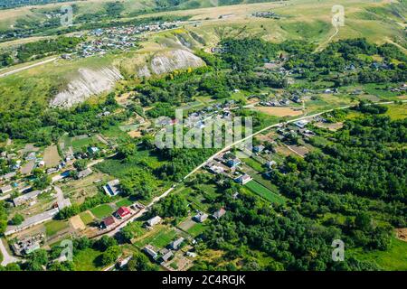 Ländliche Dorf zwischen grünen Hügeln und landwirtschaftlichen Feldern in der Landschaft, Luftbild von Drohne. Stockfoto