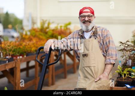 Waist up Porträt von fröhlichen Senior Gärtner Blick auf Kamera, während auf Schaufel lehnen genießen Arbeit auf Plantage im Freien, kopieren Raum Stockfoto