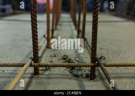 Nahaufnahme und selektive Fokusansicht der Stahlstäbe der Fundamentverstärkung auf nassem Zementboden, Struktur auf einer Baustelle im Innenbereich. Stockfoto