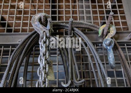 Hebehaken mit Sicherheitsriegel, Stahlseile und Metall-Industrieketten auf Eisengewebe, Betonwerk Fabrik Werkzeuge Lagerung. Stockfoto