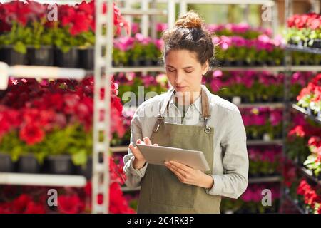 Taille up Porträt der modernen jungen Frau mit digitalen Tablet umgeben von schönen Blumen, während die Arbeit in Plantage im Freien genießen, kopieren Raum Stockfoto