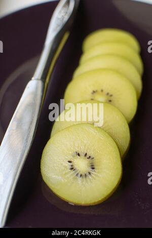 Goldene Kiwis in Scheiben geschnitten, neben einem Messer liegend Stockfoto