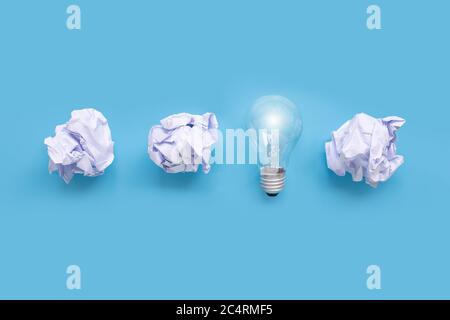Glühbirne mit weißer zerknitterter Papierkugel auf blauem Hintergrund. Draufsicht Stockfoto