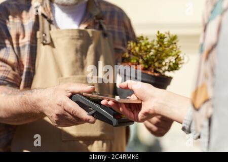 Nahaufnahme einer nicht erkennbaren Kundin, die ihre Bankkarte hält, während sie über NFC in Plantage im Freien bezahlt, Platz zum Kopieren Stockfoto