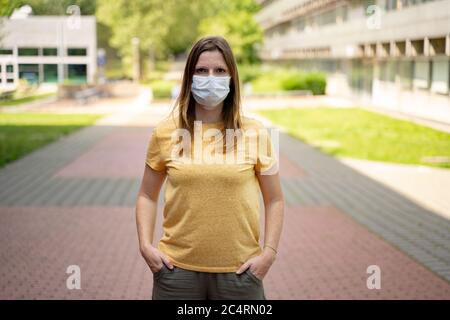 Frau in Freizeit Kleidung trägt Einweg-Schutz Gesichtsmaske auf bunten Bürgersteig stehen. Corona-Virus-Pandemieschutzkonzept. Stockfoto