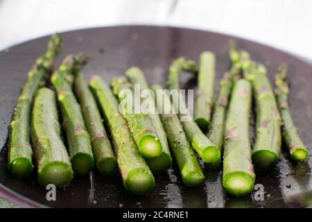 Würzigen grünen Spargel in der Hälfte liegend auf einem violetten Teller geschnitten Stockfoto