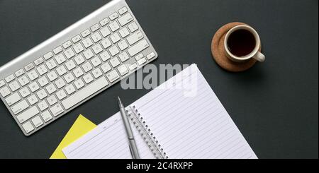 Draufsicht auf Bürotisch mit kabelloser Tastatur, Kaffee, Notizblock und Stift. Stockfoto