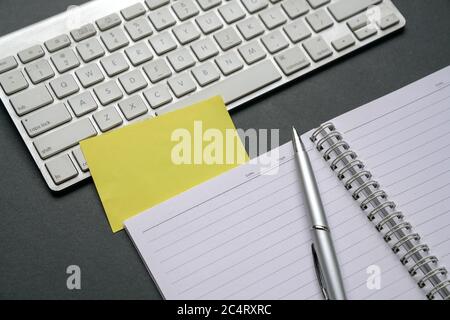 Draufsicht auf Bürotisch mit Computertastatur, Notizblock, Stift und leerem gelben Papier. Stockfoto