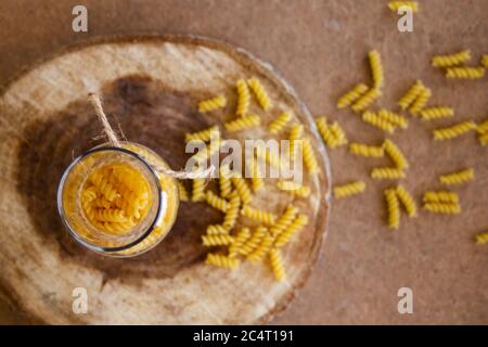 Spirale Pasta in einem Glas auf einem Holzständer, verstreut auf dem Tisch Stockfoto