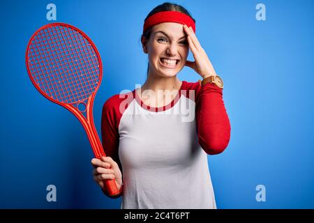 Junge schöne Rotschopf Sportlerin Tennis spielen mit Schläger über blauem Hintergrund betont mit Hand auf Kopf, schockiert mit Scham und Überraschung Gesicht, Stockfoto