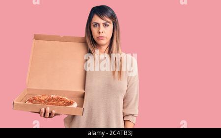 Junge schöne Frau hält Lieferung Karton mit Pizza Denken Haltung und nüchternen Ausdruck selbstbewusst suchen Stockfoto