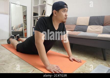 Asiatische männliche tun Übung zu Hause, um gesund zu bleiben auf neue normale Lebensweise, Indoor-Home-Workout-Konzept, Stretching für Flexibilität Stockfoto