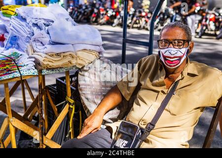 Street alten männlichen Verkäufer von Geschirrtüchern und Boden Lumpen tragen eine lustige Clown Gesichtsmaske mit einem Lächeln, während der Covid-19 Pandemie. Stockfoto