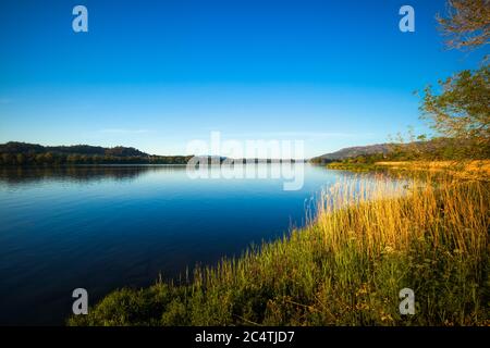 Langer Fluss, umgeben von Grün und Bergen, die unter dem glitzern Blauer Himmel Stockfoto