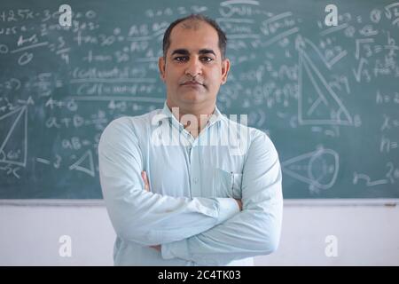 Portrait von ernsthaften männlichen Lehrer, der gegen Tafel steht und Mathematik im Klassenzimmer, Schule und Bildungskonzept unterrichtet. Stockfoto