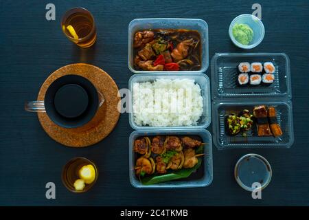 Asiatische Küche, Sushi, Brötchen, Reis und Hähnchenspieße. Essen in Einweggeschirr. Bestellen Sie asiatische Speisen zu Hause. Stockfoto