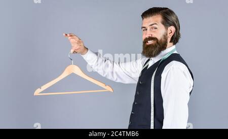 Portrait des Mannes hält Kleiderbügel. Schneider Mann verwenden Maßband. Professionelle männliche sartor mit Maßband und Kleiderbügel. Schöner Mann in smart Freizeitkleidung hält Kleiderbügel. Stockfoto