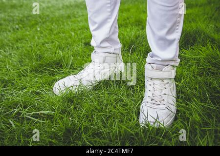 Männliche Füße in weißen Schuhen auf grünem Gras. Weiße Jeans. Stockfoto
