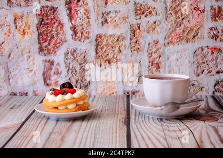 Biskuit Honigkuchen mit Sahne, Kirsche und Erdbeeren steht auf einem Holztisch, neben einer Tasse Tee. Nahaufnahme. Stockfoto