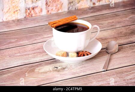 Eine Tasse schwarzen Kaffee auf einer Untertasse mit Zimt, Anis und Rohrzuckerscheiben. Nahaufnahme. Stockfoto