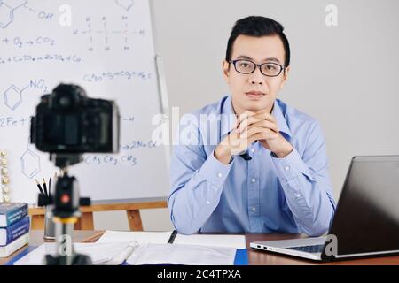 Selbstbewusster junger Wissenschaftslehrer, der mit einem geöffneten Laptop am Schreibtisch sitzt und Online-Chemieunterricht veranstaltet Stockfoto