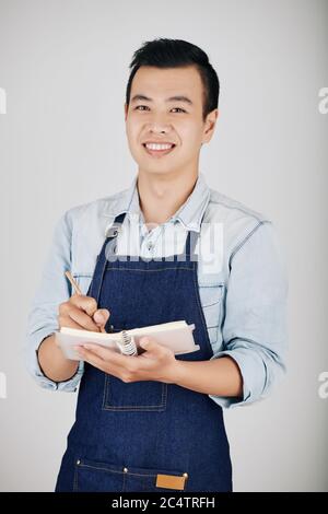 Porträt eines lächelnden jungen Kellners, der Notizen in Notizbücher gemacht hat Stockfoto
