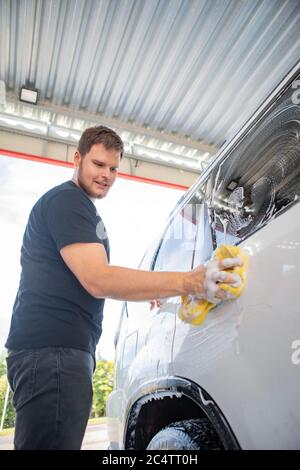 Man-Reinigungswagen mit gelbem Schwamm. Carwash-Konzept Stockfoto