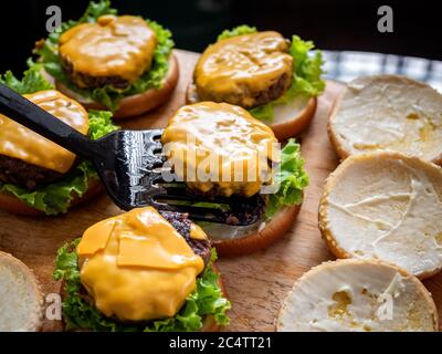 Leckere hausgemachte saftige Burger. Hand mit Spatel Putting Beef Cover mit Käse auf frischen grünen Salat auf Holztisch, Prozess der Herstellung von köstlichen Hause Stockfoto