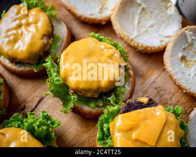 Leckere hausgemachte saftige Burger. Käse auf Rindfleisch, frischer grüner Salat auf Holztisch, Prozess der Herstellung von leckeren hausgemachten Burger. Stockfoto