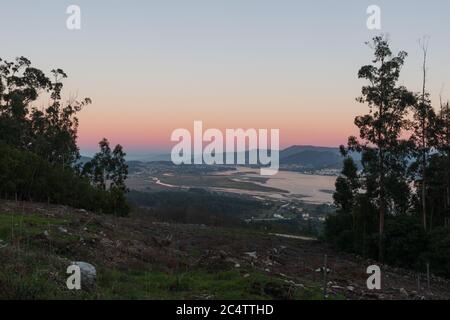 Langer Fluss, umgeben von hohen Bergen, die unter dem Blau schimmern Und rosa Himmel Stockfoto