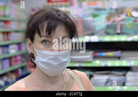 Junge Frau mit einer medizinischen Maske in einem Supermarkt und Blick auf die Kamera. Das Konzept des Schutzes gegen Coronavirus und andere respiratorische Stockfoto