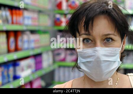 Junge Frau mit einer medizinischen Maske in einem Supermarkt und Blick auf die Kamera. Das Konzept des Schutzes gegen Coronavirus und andere respiratorische Stockfoto