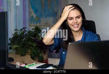 Verwirrte junge Frau arbeitet online mit einem Laptop im Büro am Schreibtisch oder zu Hause und hält ihre Hand über den Kopf Stockfoto