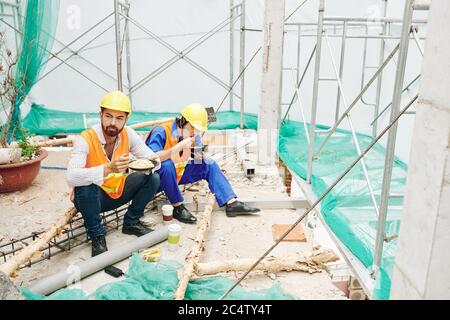 Ingenieur und Baumeister beim Mittagessen auf der Baustelle, Essen Nudeln, Salat und Kaffee Stockfoto