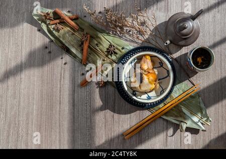 Chinesische Reisknödel (Zongzi) geformt pyramidal von Blättern Zutaten auf Schüssel chinesischen Stil und Essstäbchen mit chinesischem Tee verpackt. Berühmt als Stockfoto