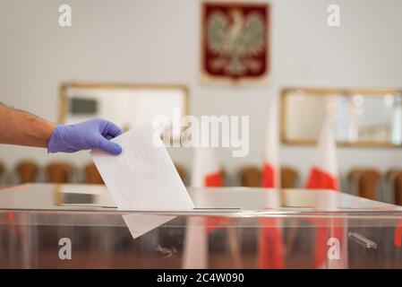 Werfen einer Karte mit einer Stimme an die Wahlurne während der Wahlen. Im Hintergrund polieren Emblem und Flagge Stockfoto