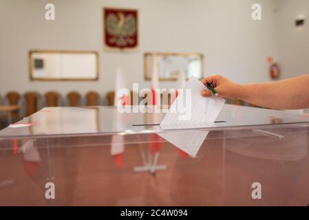 Werfen einer Karte mit einer Stimme an die Wahlurne während der Wahlen. Im Hintergrund polieren Emblem und Flagge Stockfoto